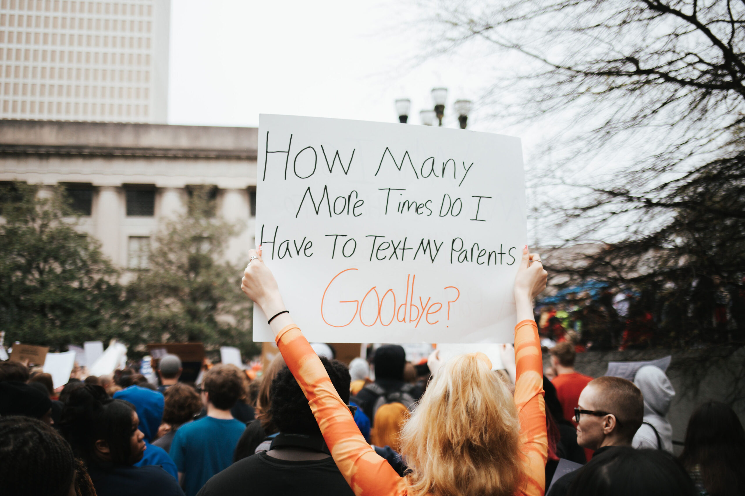 Student holds up sign reading "How many more times do I have to text my parents goodbye?"